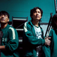 Cast members of Squid Game inside looking anxious at something off screen and preparing to run or fight.